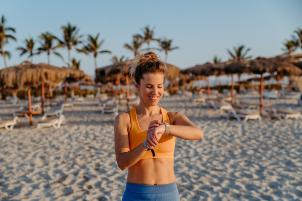 Close-up of young sportive woman at the beach, checking at smartwatch.