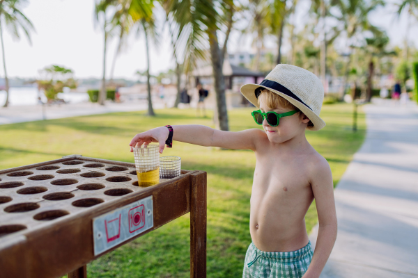 Little boy putting down his drink at storage table on a beach.