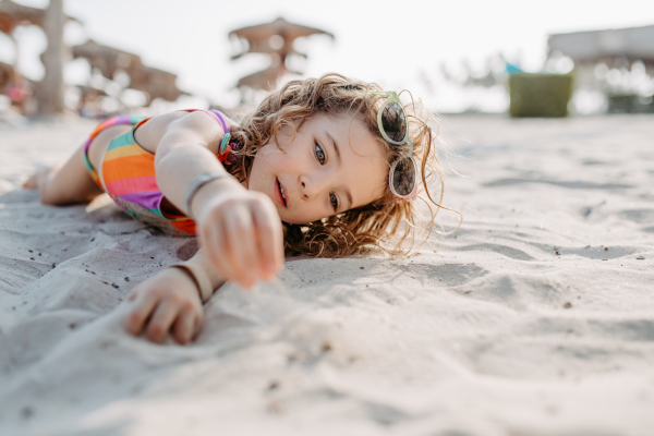 Little girl playing on the beach, lying in sand.