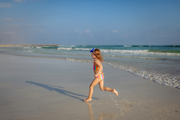 Little girl in swimsuit running out of sea, enjoying summer holiday.