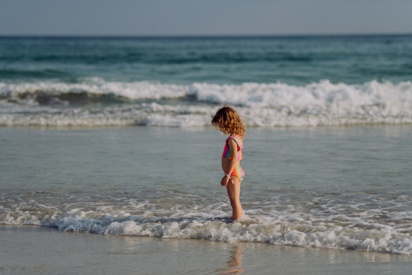 Little girl in swimsuit standing in the sea, enjoying summer holiday.