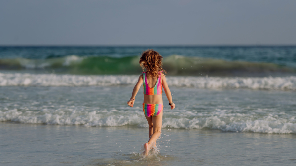 Little girl in swimsuit running in the sea, enjoying summer holiday.