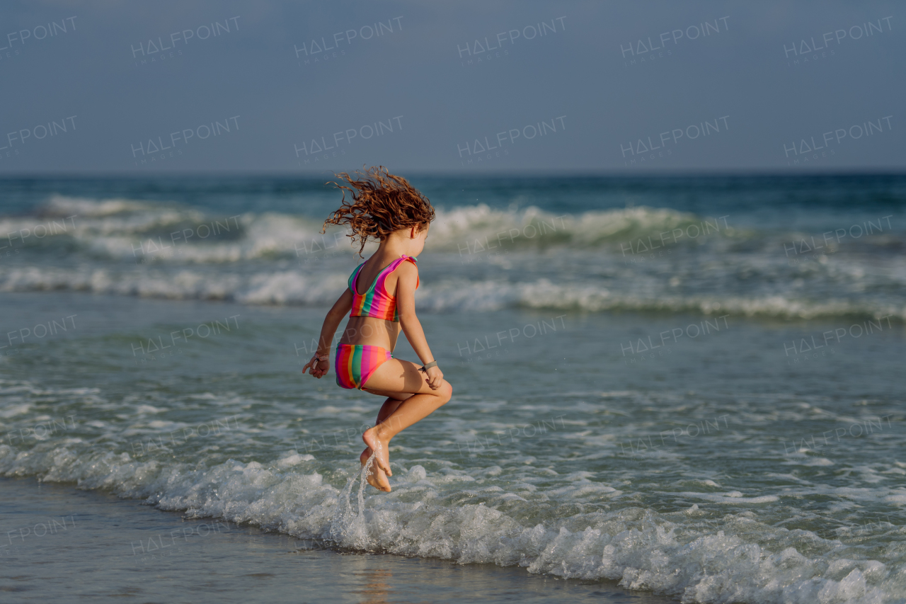 Little girl in swimsuit jumping in the sea, enjoying summer holiday.