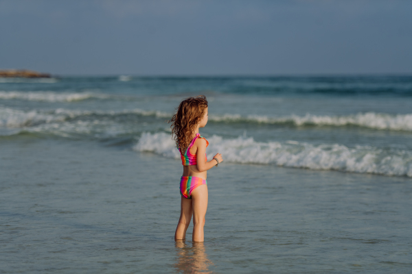 Little girl in swimsuit standing in the sea, enjoying summer holiday.