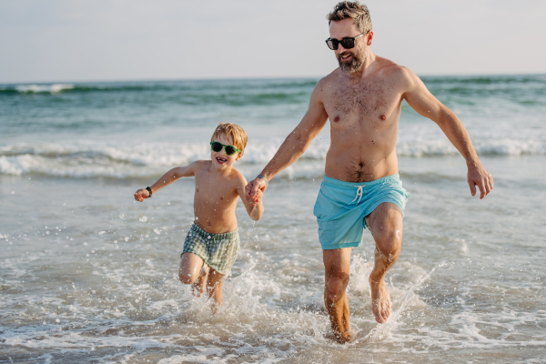 Father with his little son running out of sea, enjoying summer vacation.