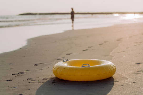 Close-up of yellow inflatable wheel on the beach, with person in the background.