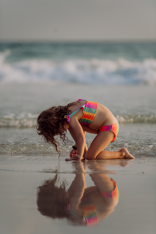 Little girl looking for shells on a beach, enjoying exotic vacation.