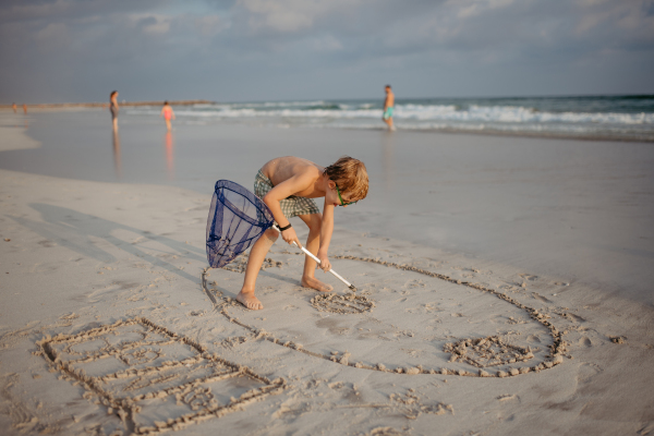 Little boy playing and drawing in a sand with a fishing net, enjoying holiday time.