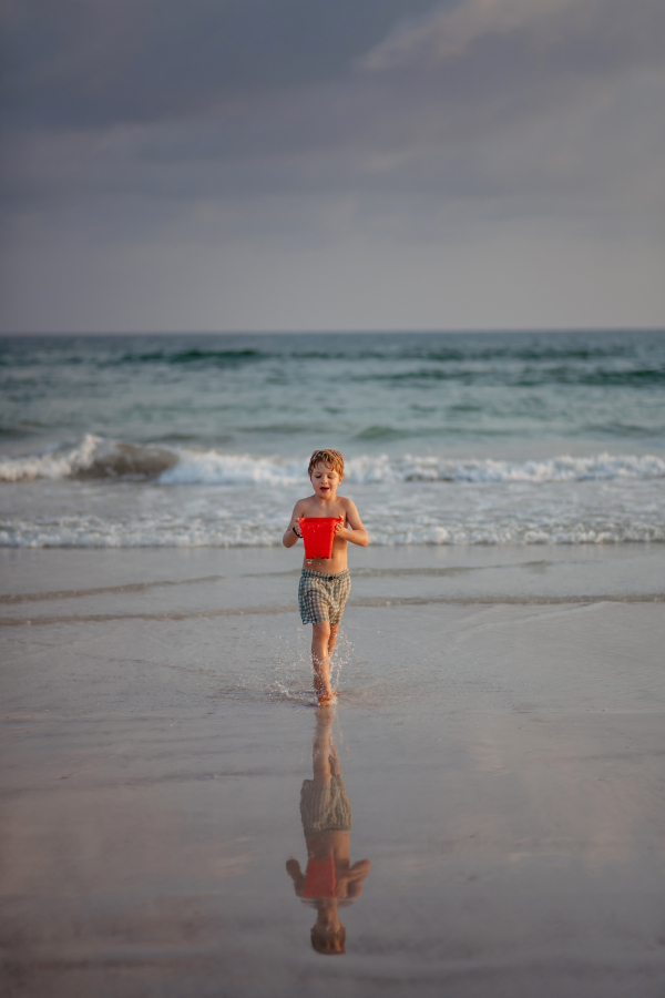 Little boy in swimsuit running out of sea, enjoying summer holiday.