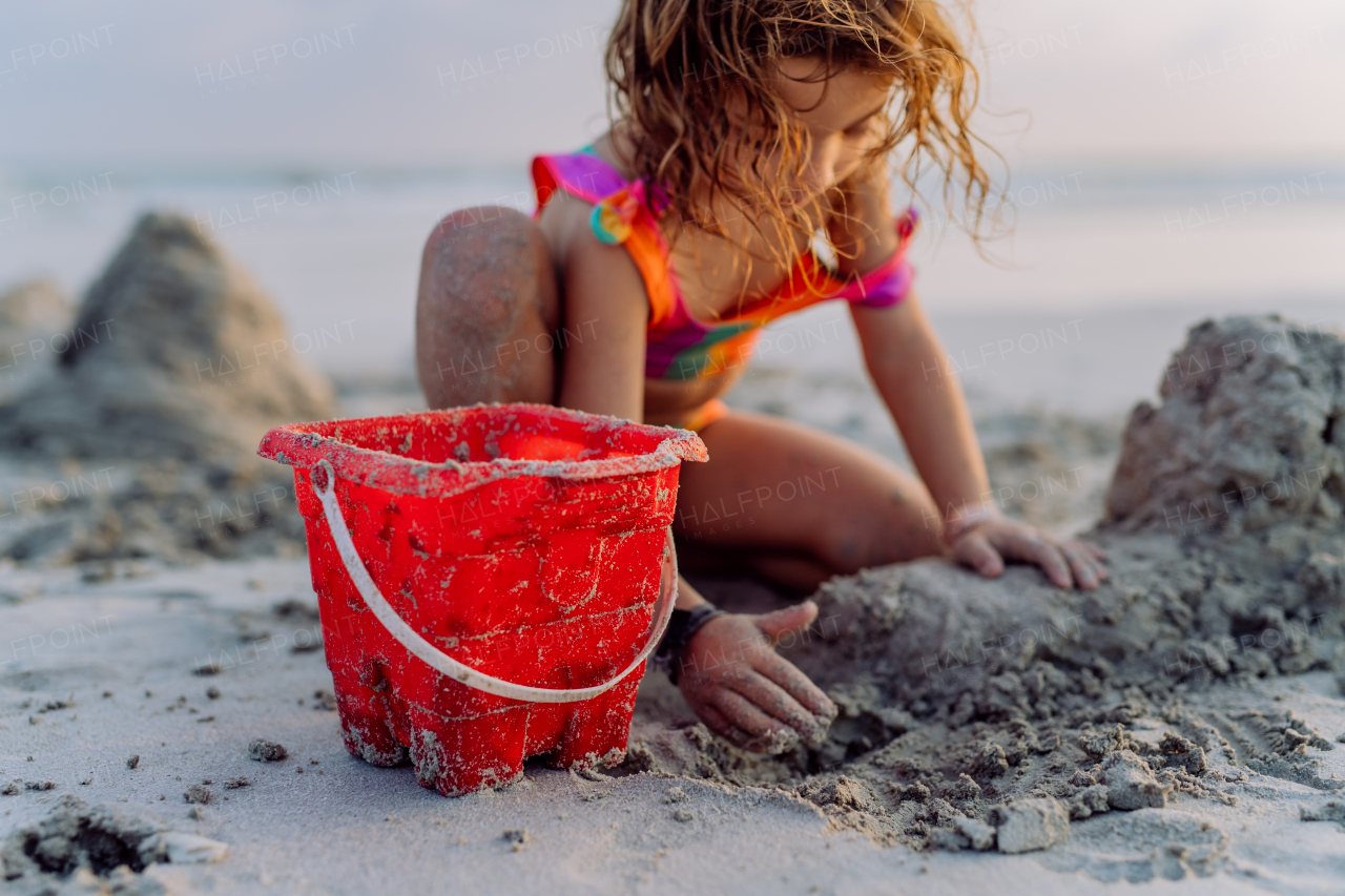 Little girl playing on the beach, building a sand castle.