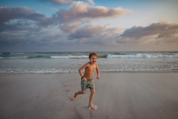 Little boy in swimsuit running out of sea, enjoying summer holiday.