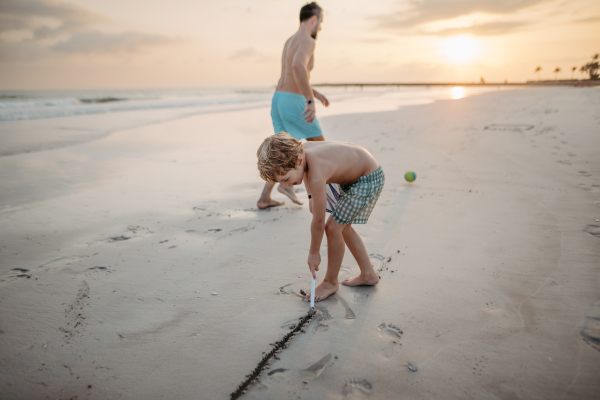 Little boy playing and drawing in a sand with a fishing net, preparing for football playing with his father.