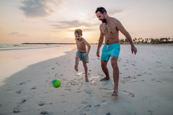 Father with his son plaing football on a beach.