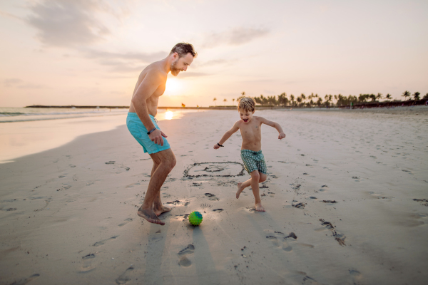 Father with his son plaing football on a beach.