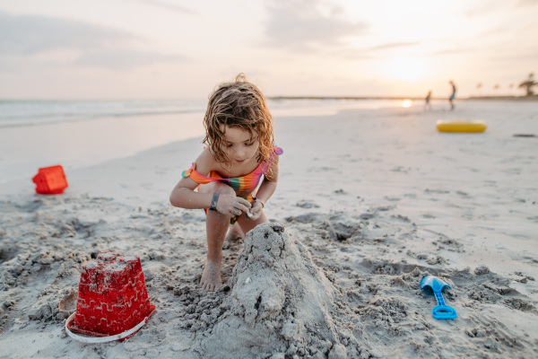 Little girl playing on the beach, building a sand castle.