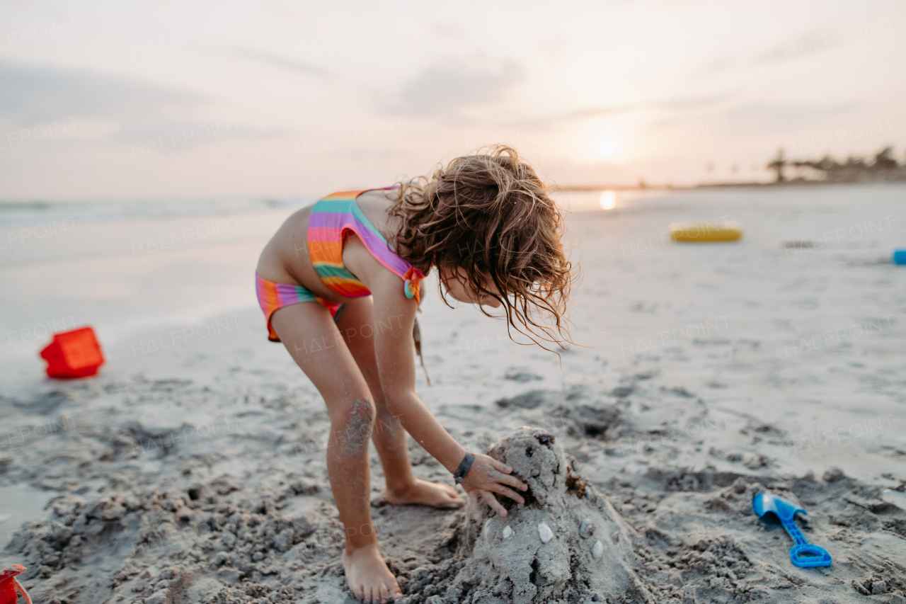 Little girl playing on the beach, building a sand castle.