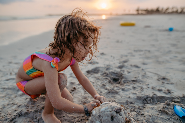 Little girl playing on the beach, building a sand castle.