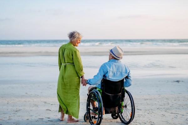 Senior man on wheelchair enjoying together time with his wife at the sea.