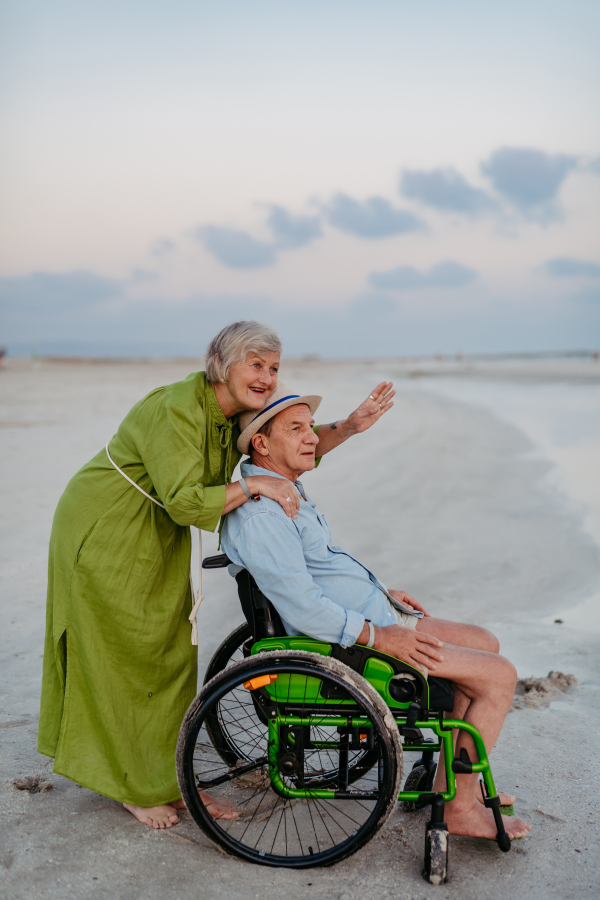 Senior man on wheelchair enjoying together time with his wife at the sea.