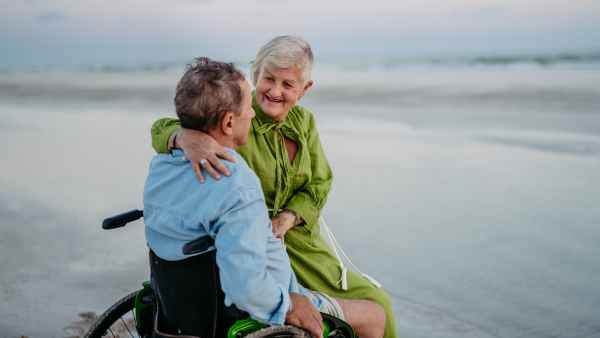 Senior man on wheelchair enjoying together time with his wife at the sea.