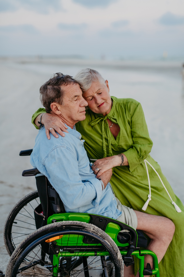 Senior man on wheelchair enjoying together time with his wife at the sea.