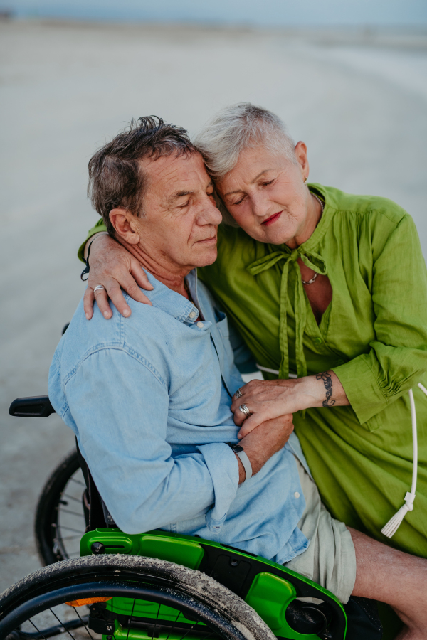 Senior man on wheelchair enjoying together time with his wife at the sea.