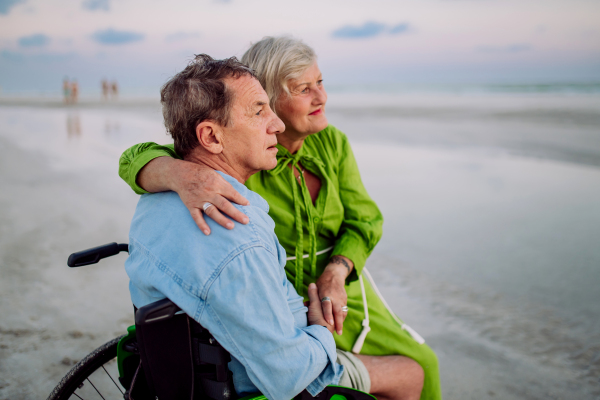 Senior man on wheelchair enjoying together time with his wife at the sea.