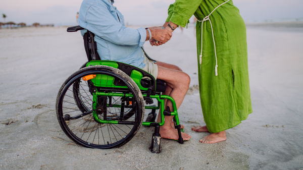 Senior man on wheelchair enjoying together time with his wife at the sea, low section.