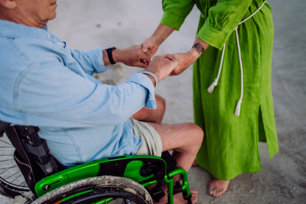 Close-up of senior woman holding hands her husband on wheelchair and enjoying vacations together.