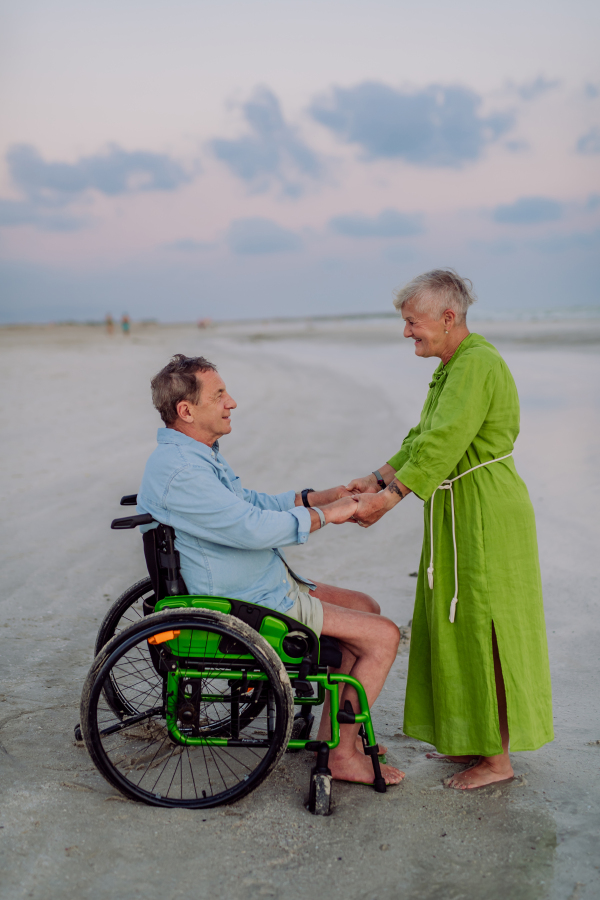 Senior man on wheelchair enjoying together time with his wife at the sea.