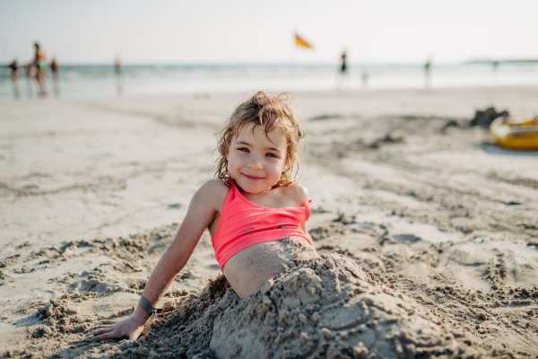 Little girl buring herself in sand, enoying exotic summer vacation at sea.