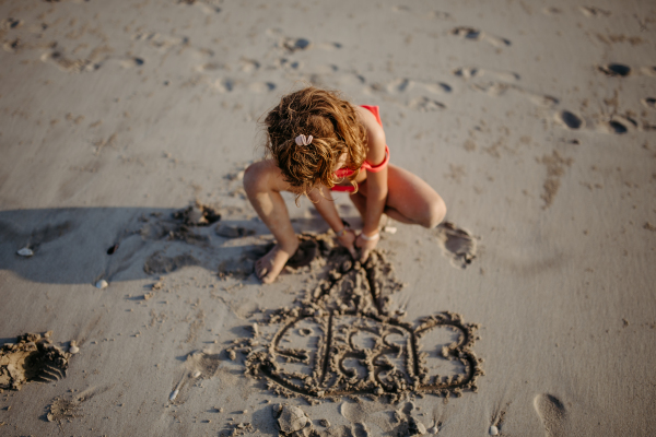 Little girl drawing in sand on beach during summer holliday.