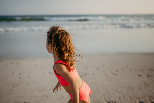 Little girl in swimsuit running running on the beach, enjoying summer holiday.