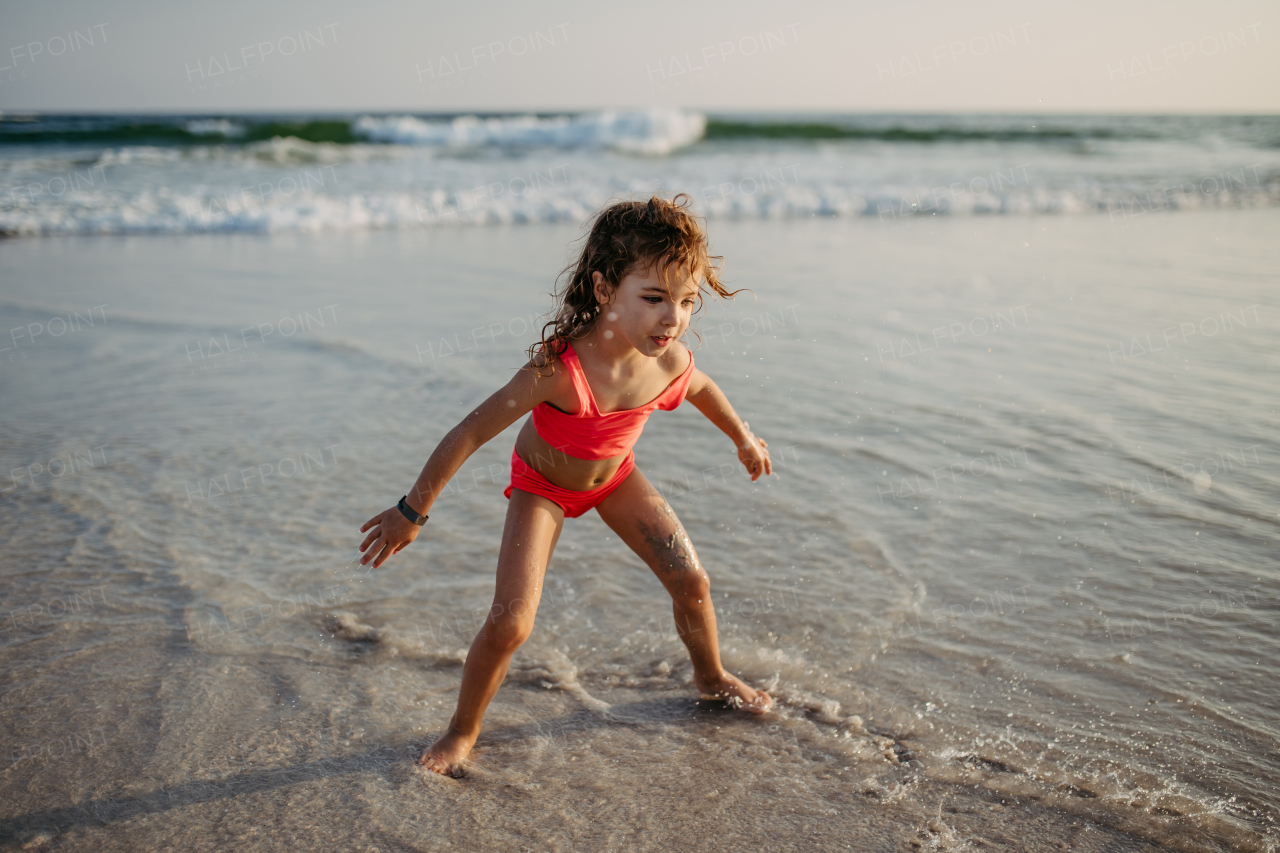 Little girl in swimsuit running running on the beach, enjoying summer holiday.