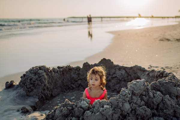 Little girl playing on the beach, digging hole in the sand.