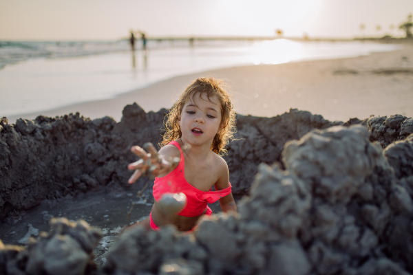 Little girl playing on the beach, digging hole in the sand.