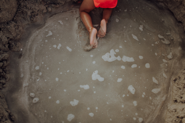 Top view of little girl playing on the beach, digging hole in the sand.