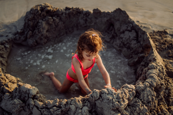 Little girl playing on the beach, digging hole in the sand.