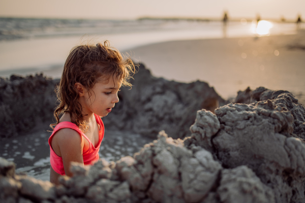 Little girl playing on the beach, digging hole in the sand.