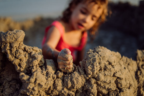 Little girl playing on the beach, digging hole in the sand.