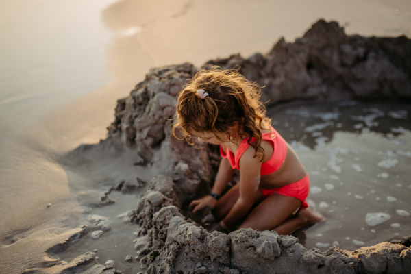 Little girl playing on the beach, digging hole in the sand.