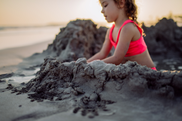 Little girl playing on the beach, digging hole in the sand.