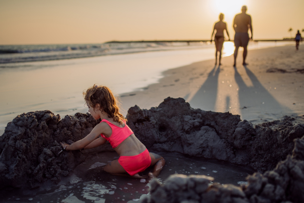 Little girl playing on the beach, digging hole in the sand.