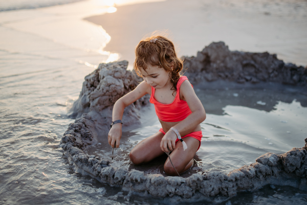 Little girl playing on the beach, digging hole in the sand.