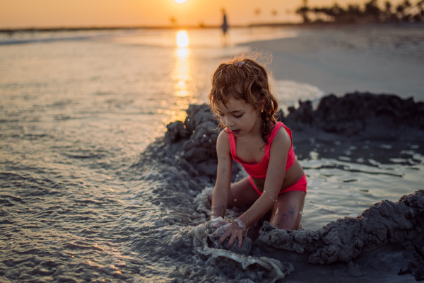 Little girl playing on the beach, digging hole in the sand.