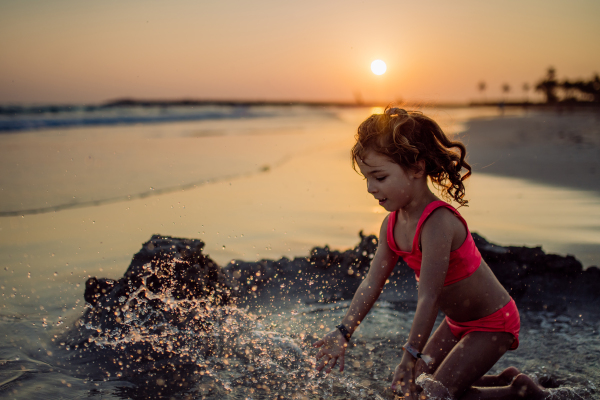 Little girl playing on the beach, digging hole in the sand.