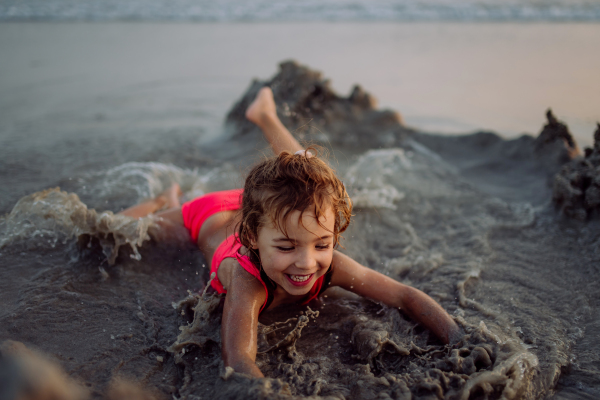 Little girl playing on the beach, digging hole in the sand.