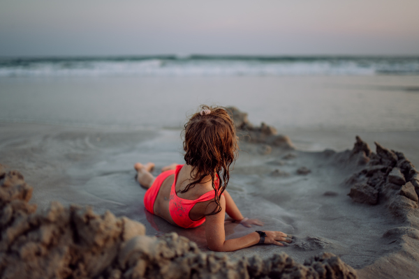 Little girl playing on the beach, digging hole in the sand.