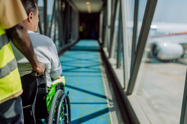 Rear view of an airport worker pushing man on wheelchair in the airplane. Concept of barrier-free travelling.