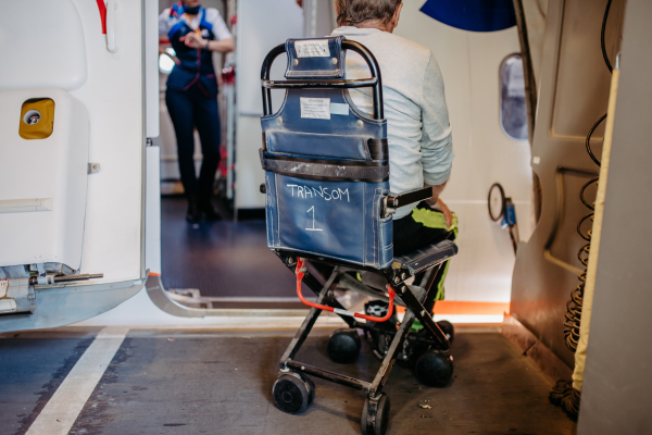 Rear view of an airport worker pushing man on wheelchair in the airplane. Concept of barrier-free travelling.